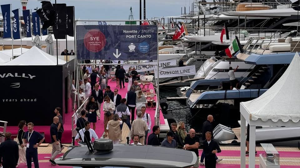 Visitors on the pink carpet at the Cannes Yachting Festival, superyachts moored alongside and the Port Canto shuttle sign overhead